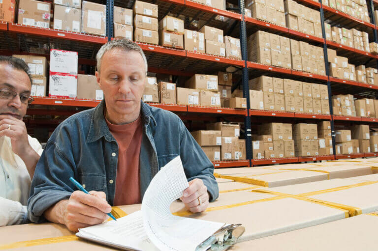 A male causcasian warehouse worker and an Hispanic American warehouse worker checking inventory in a