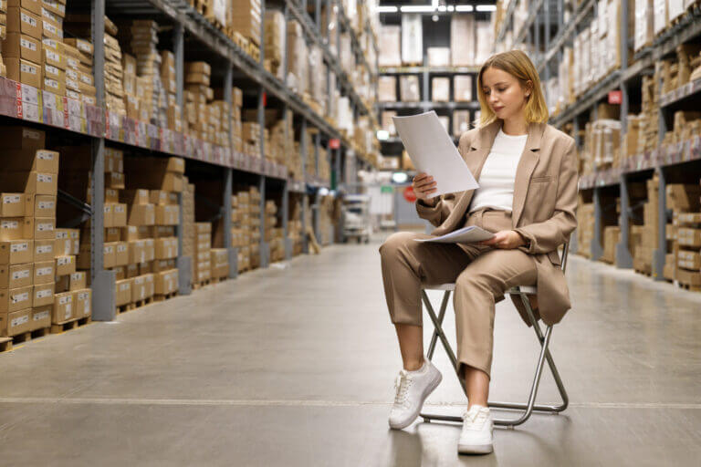 business woman or supervisor checking documents, sitting on chair at facility storage warehouse.